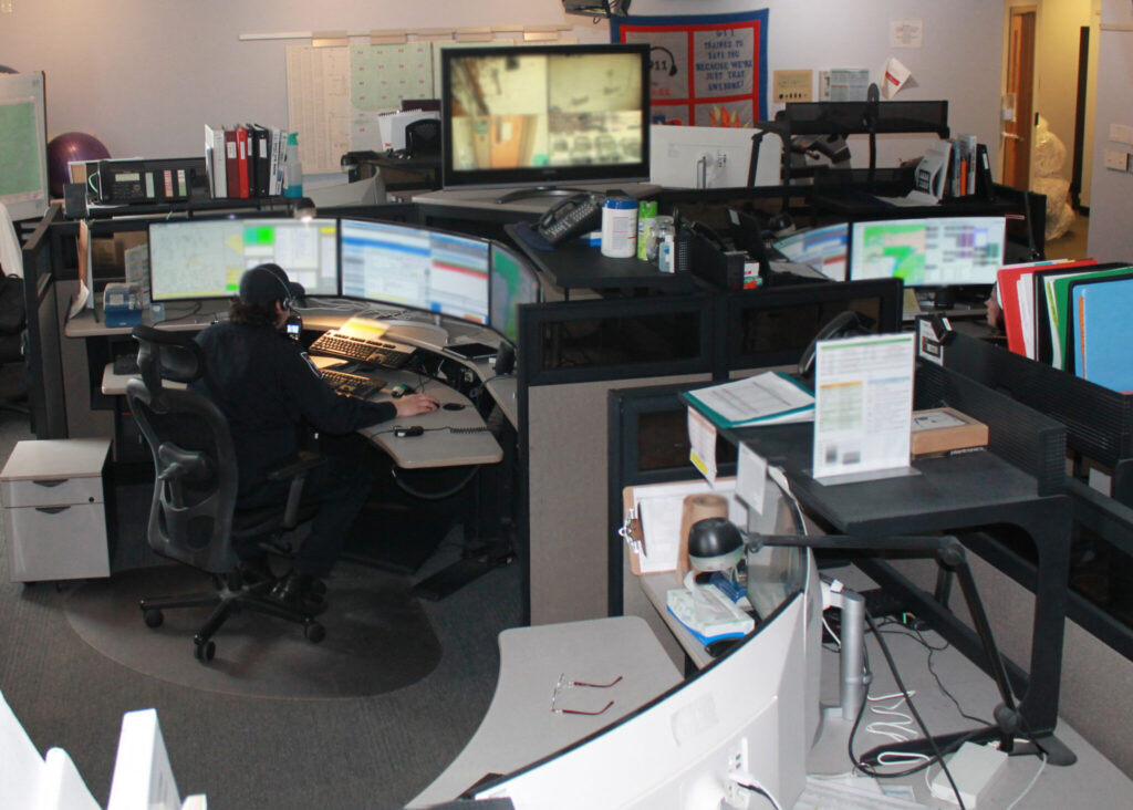 A room in a dispatch centre that shows a dispatcher sitting at a console with curved monitors in front of them.